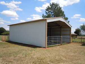 A horse barn with a metal roof in the middle of a field.