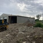 A bulldozer sits in the dirt next to a building.