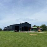 A black barn in the middle of a grassy field.