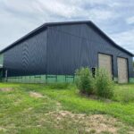 A black barn with green siding in the middle of a grassy field.
