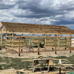 A wooden barn being built in a field.