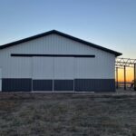 A barn in the middle of a field at sunset.