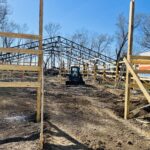 A barn under construction with a tractor in the background.
