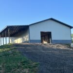 A white barn with a dirt road in the background.