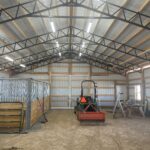 The inside of a horse barn with a tractor in it.